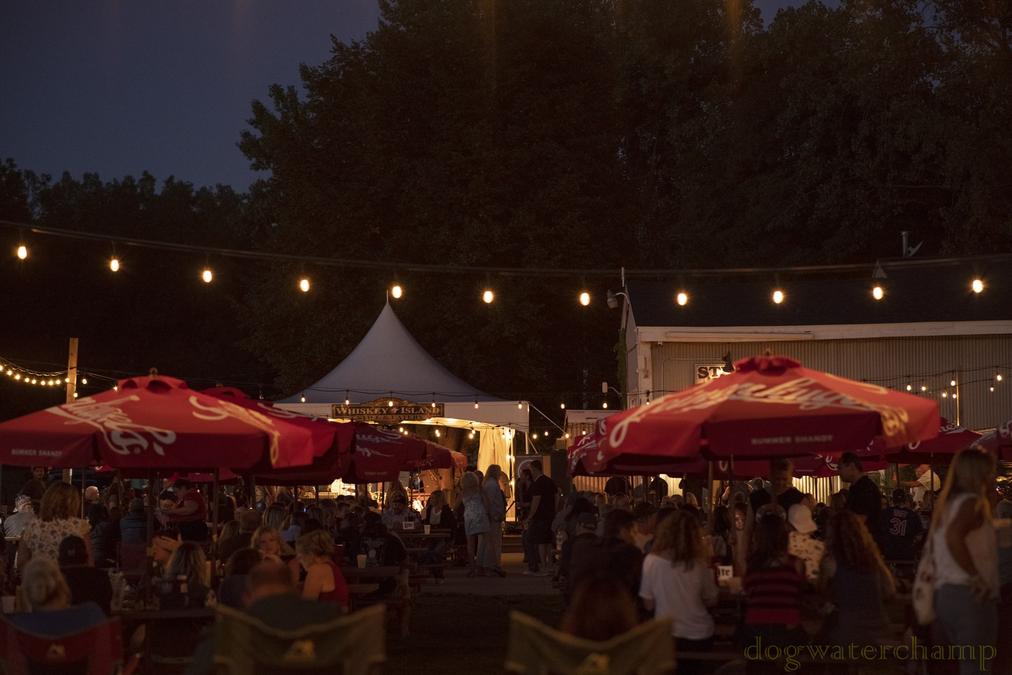 People gathering beneath string lights on the Whiskey Island patio